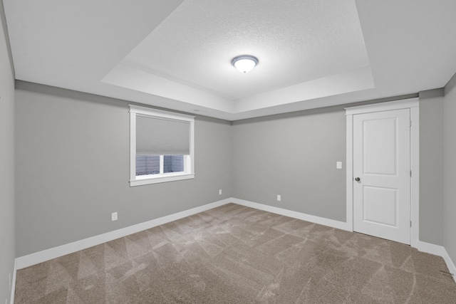 unfurnished room with a textured ceiling, carpet flooring, and a tray ceiling