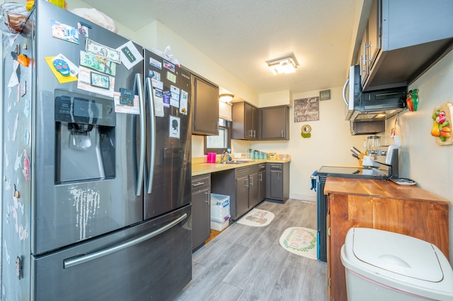 kitchen with sink, a textured ceiling, appliances with stainless steel finishes, and light hardwood / wood-style flooring