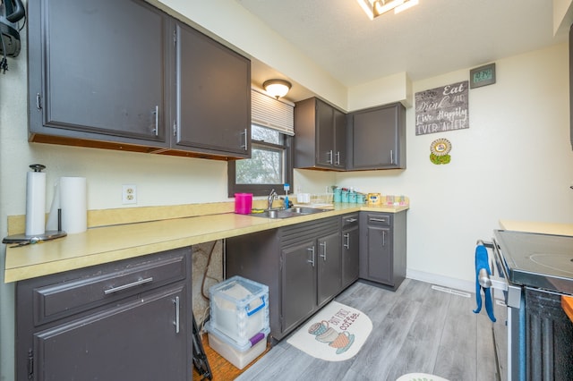 kitchen with light hardwood / wood-style floors, a textured ceiling, stove, and sink