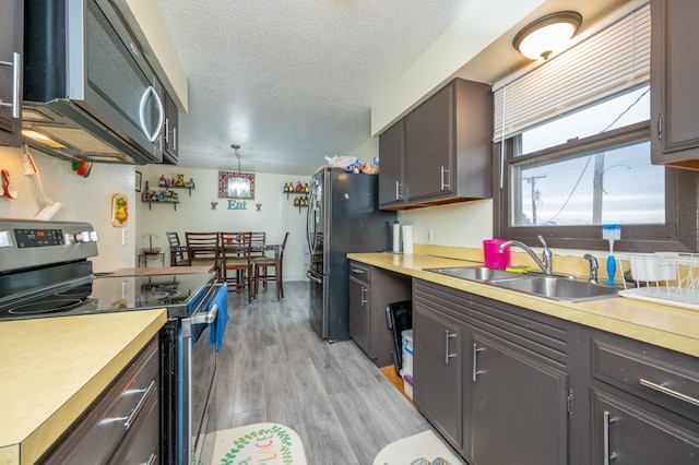 kitchen with appliances with stainless steel finishes, sink, light wood-type flooring, a textured ceiling, and pendant lighting