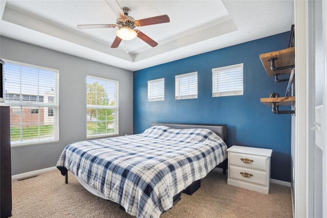 carpeted bedroom featuring a raised ceiling and ceiling fan