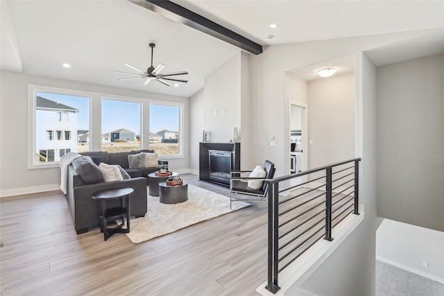 living area featuring vaulted ceiling with beams, a fireplace, wood finished floors, and baseboards