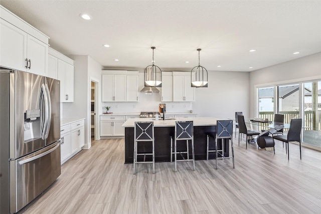 kitchen with light wood-type flooring, light countertops, stainless steel fridge, and a kitchen bar