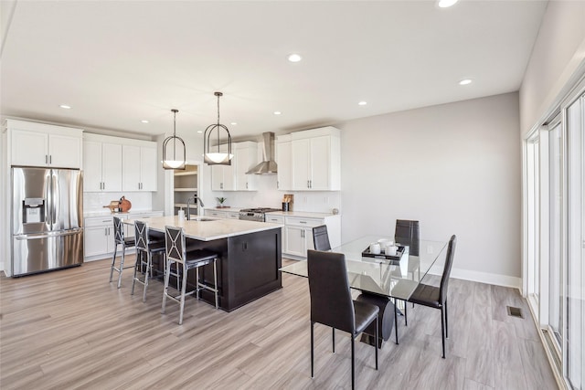 kitchen featuring a center island with sink, visible vents, appliances with stainless steel finishes, wall chimney range hood, and a sink