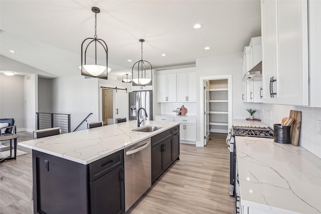 kitchen featuring a barn door, white cabinets, stainless steel appliances, light wood-type flooring, and a sink