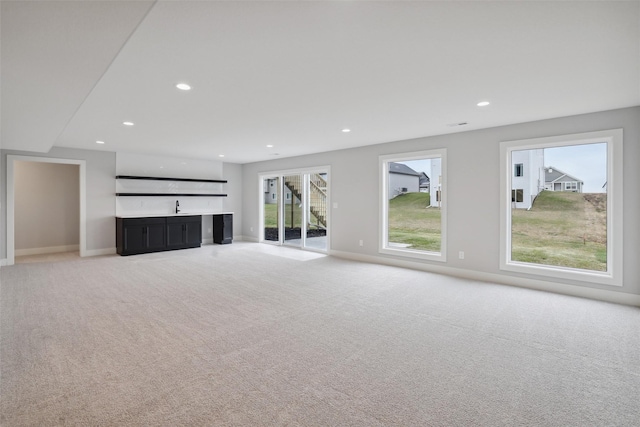 unfurnished living room featuring recessed lighting, light carpet, a sink, and baseboards