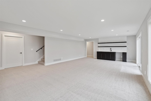 unfurnished living room featuring recessed lighting, light carpet, visible vents, baseboards, and stairs