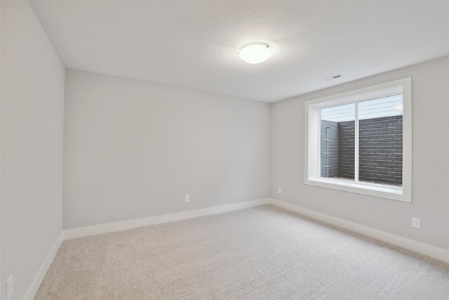 spare room featuring a textured ceiling, carpet, visible vents, and baseboards