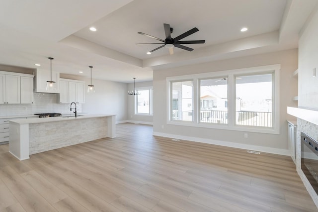 kitchen featuring a raised ceiling, hanging light fixtures, sink, and white cabinets