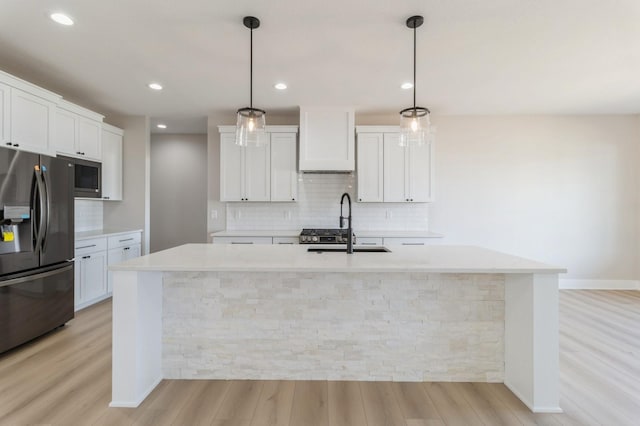 kitchen with decorative light fixtures, a kitchen island with sink, white cabinets, and stainless steel fridge with ice dispenser