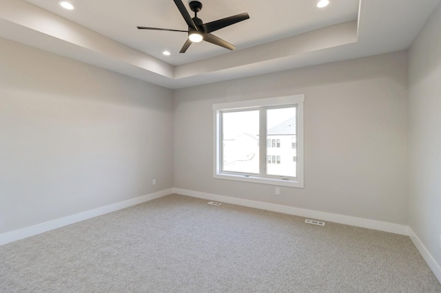 unfurnished room featuring a raised ceiling, carpet, and ceiling fan