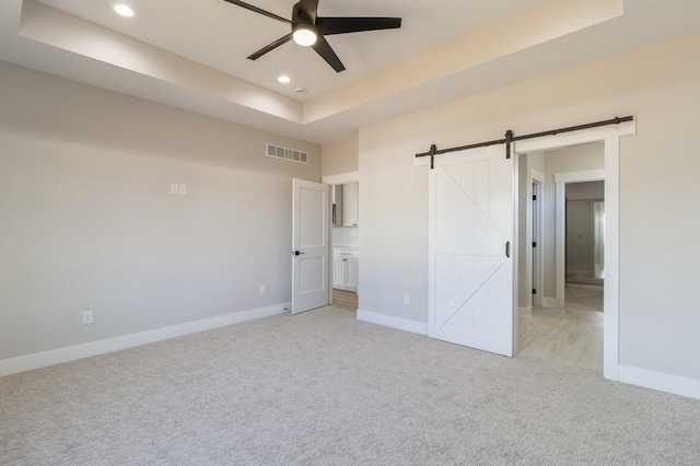 unfurnished bedroom with a barn door, a raised ceiling, and light carpet