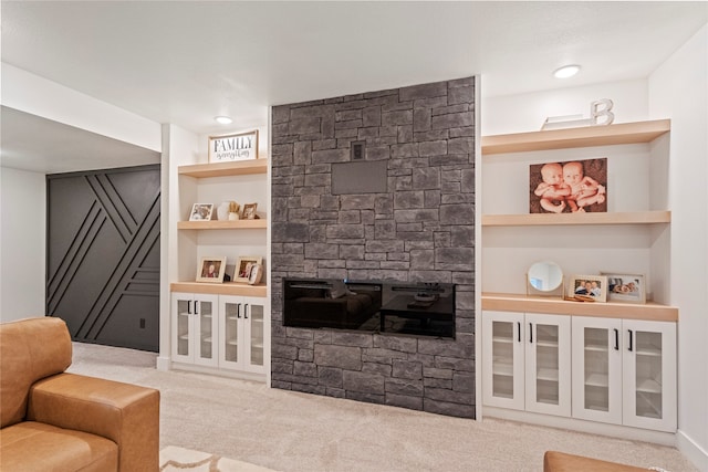 living room with built in shelves, a stone fireplace, and light colored carpet