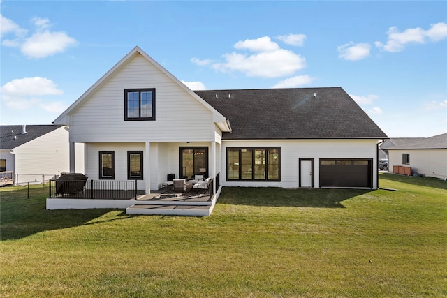 rear view of property featuring a deck, a garage, and a lawn