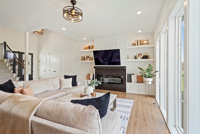 living room with built in features, light hardwood / wood-style floors, a brick fireplace, and plenty of natural light