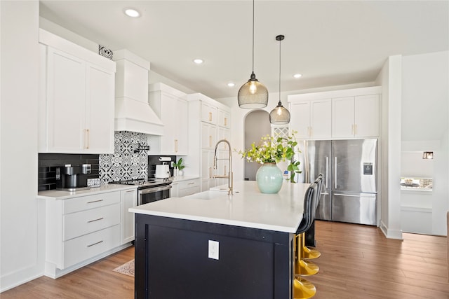 kitchen with white cabinetry, hanging light fixtures, stainless steel fridge, hardwood / wood-style floors, and an island with sink