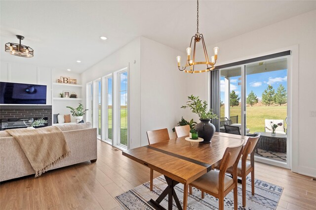 dining space with built in features, light wood-type flooring, a fireplace, and an inviting chandelier