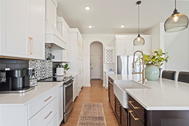 kitchen with stainless steel appliances, decorative light fixtures, white cabinets, light hardwood / wood-style floors, and an island with sink