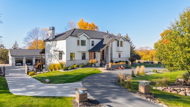 modern farmhouse style home featuring a front lawn, board and batten siding, curved driveway, and a chimney