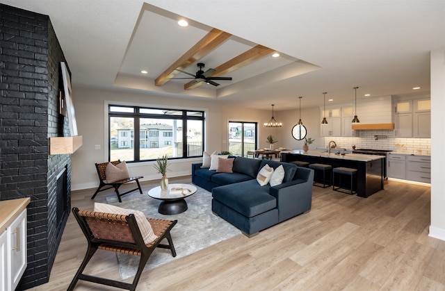 living room featuring light hardwood / wood-style floors, a raised ceiling, beamed ceiling, and a brick fireplace