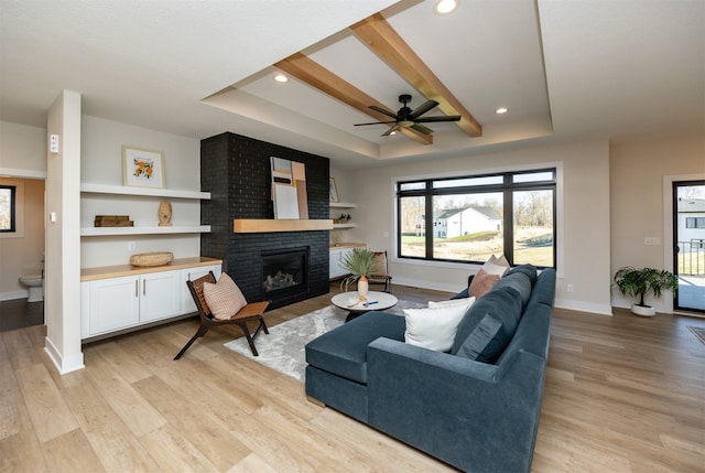 living room featuring ceiling fan, a raised ceiling, light hardwood / wood-style flooring, and a fireplace