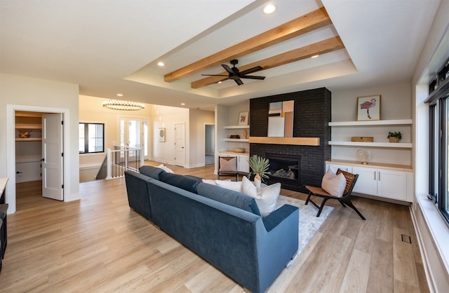 living room featuring beamed ceiling, a tray ceiling, light wood-type flooring, and a fireplace