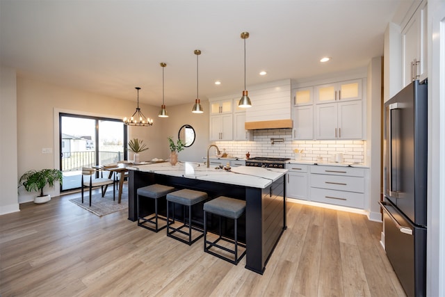 kitchen with custom range hood, stainless steel appliances, white cabinetry, and an island with sink