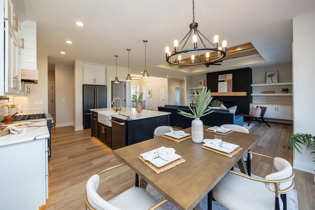 dining area featuring sink, a fireplace, a tray ceiling, light hardwood / wood-style floors, and a notable chandelier