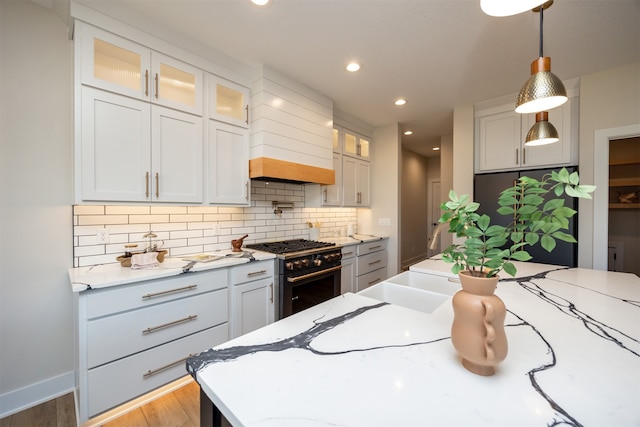 kitchen featuring custom range hood, light stone countertops, pendant lighting, appliances with stainless steel finishes, and light hardwood / wood-style floors