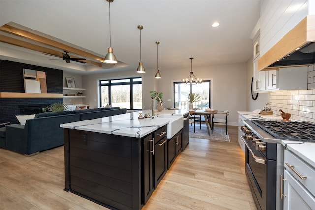 kitchen featuring high end stove, light hardwood / wood-style flooring, an island with sink, white cabinetry, and premium range hood