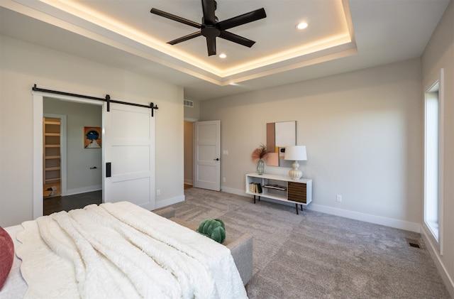 bedroom featuring light carpet, a barn door, a raised ceiling, and ceiling fan