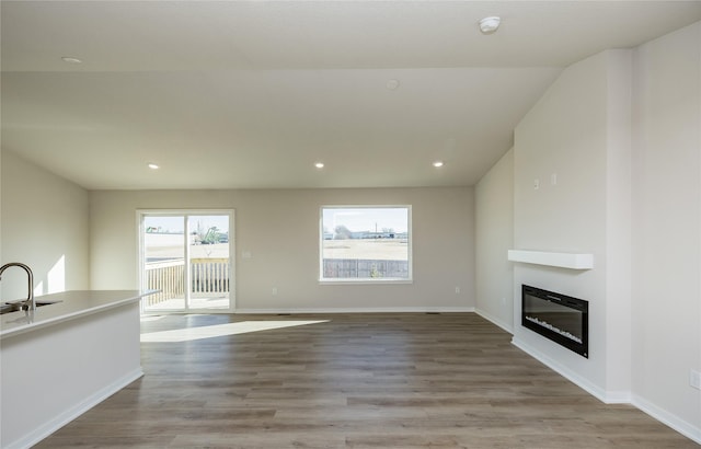 unfurnished living room featuring vaulted ceiling, sink, and light wood-type flooring