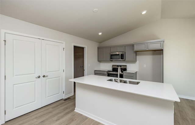 kitchen featuring vaulted ceiling, stainless steel appliances, an island with sink, and decorative backsplash