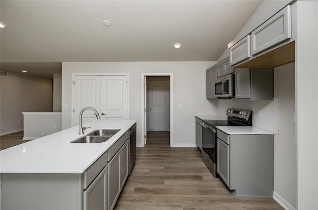 kitchen featuring gray cabinetry, sink, stainless steel appliances, and a center island with sink