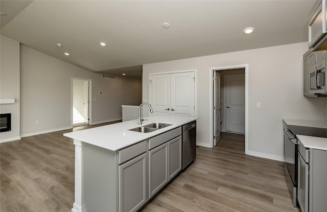 kitchen with stainless steel appliances, gray cabinets, sink, and a center island with sink