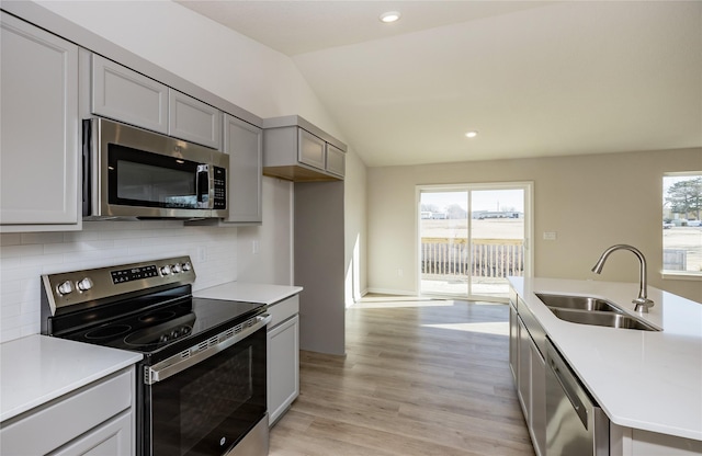 kitchen featuring sink, gray cabinetry, backsplash, stainless steel appliances, and vaulted ceiling