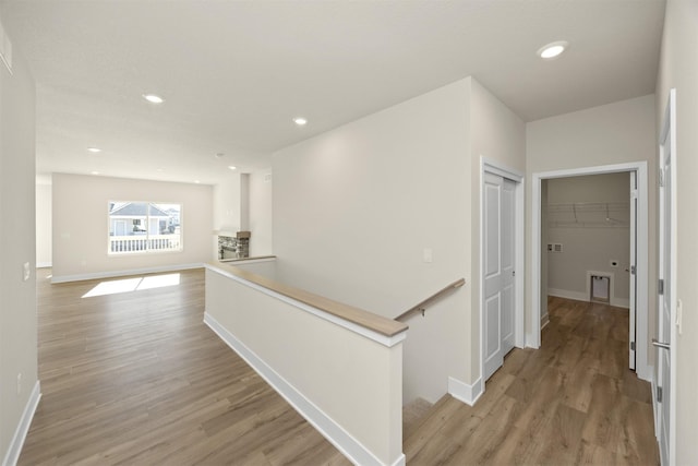 corridor with baseboards, light wood-style flooring, an upstairs landing, and recessed lighting