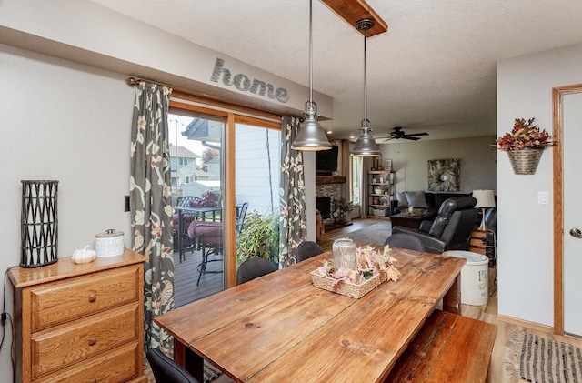 dining area with a stone fireplace, hardwood / wood-style floors, a textured ceiling, and ceiling fan