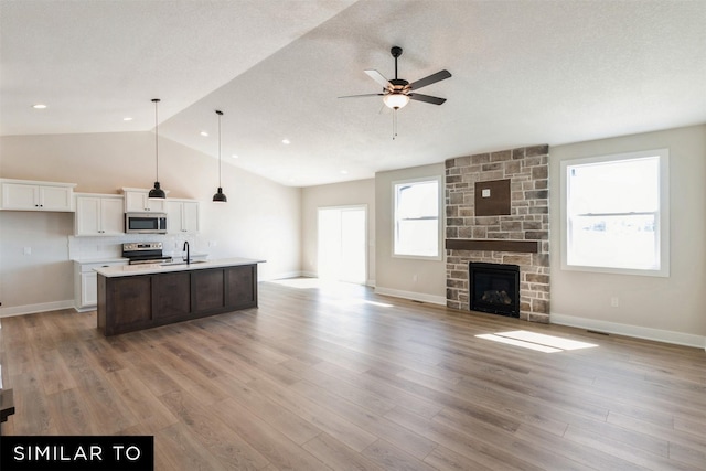 kitchen featuring decorative light fixtures, appliances with stainless steel finishes, a kitchen island with sink, light hardwood / wood-style floors, and white cabinets