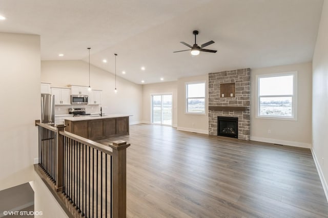 living room featuring a stone fireplace, lofted ceiling, sink, ceiling fan, and light wood-type flooring