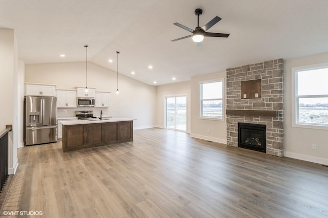 kitchen featuring hanging light fixtures, stainless steel appliances, a wealth of natural light, a fireplace, and an island with sink