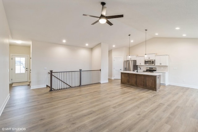 kitchen with white cabinetry, decorative light fixtures, light hardwood / wood-style flooring, appliances with stainless steel finishes, and a kitchen island with sink