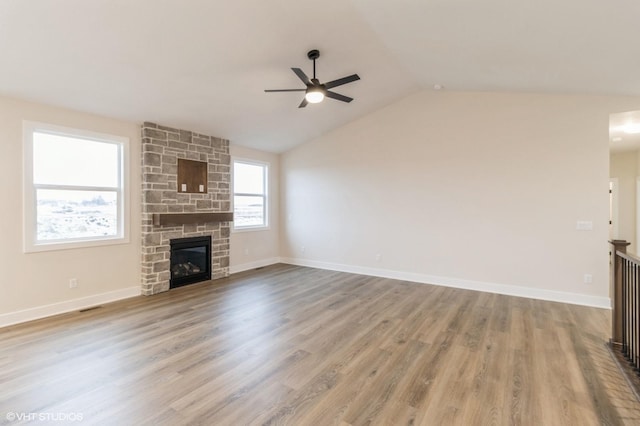 unfurnished living room featuring vaulted ceiling, a stone fireplace, hardwood / wood-style floors, and ceiling fan