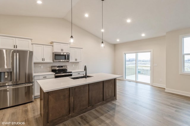 kitchen with sink, hanging light fixtures, stainless steel appliances, white cabinets, and a center island with sink