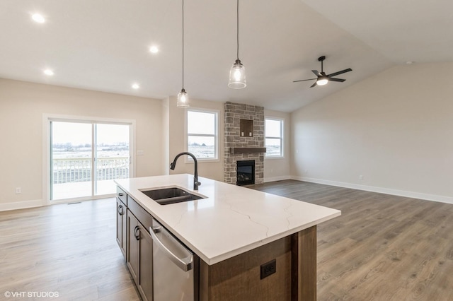 kitchen with sink, hanging light fixtures, stainless steel dishwasher, light stone countertops, and a center island with sink