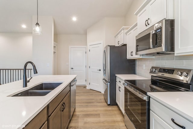 kitchen featuring stainless steel appliances, white cabinetry, sink, and decorative light fixtures