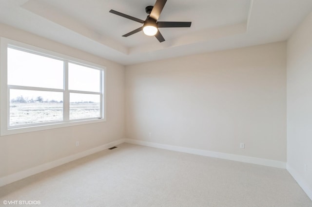 carpeted empty room with ceiling fan and a raised ceiling