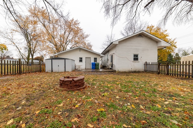 back of property featuring an outbuilding, a patio, a storage shed, a fenced backyard, and a fire pit