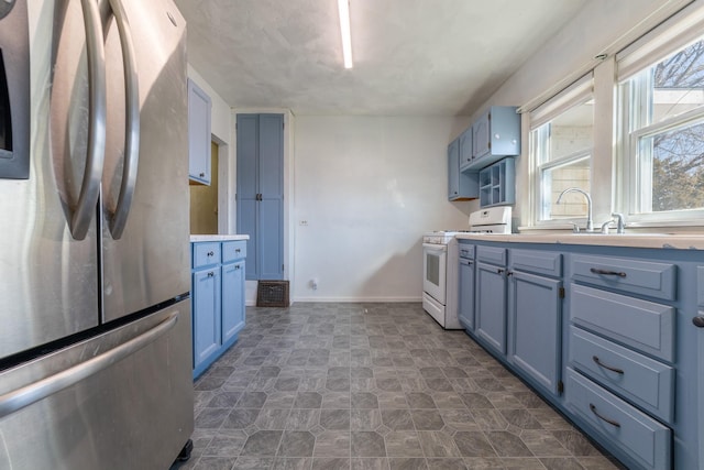 kitchen featuring blue cabinets, a sink, light countertops, freestanding refrigerator, and white gas range