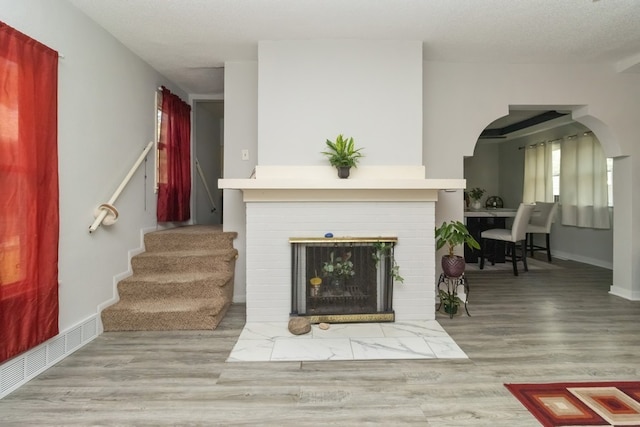 living room featuring light wood-type flooring, a textured ceiling, and a brick fireplace